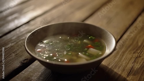 Steaming vegetable soup in a ceramic bowl on a rustic wooden table. Food advertising, recipe videos, and restaurant promotion.