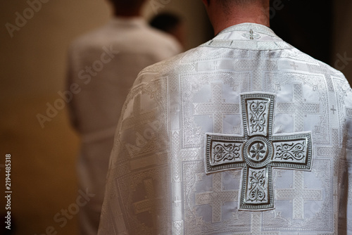 Bild auf Leinwand Priest in a white embroidered vestment with ornate cross seen from behind during