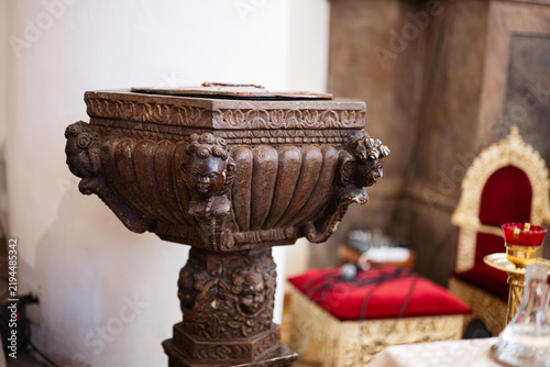 Фотография Ornate baptismal font in historic church interior with carved cherubs and red ve