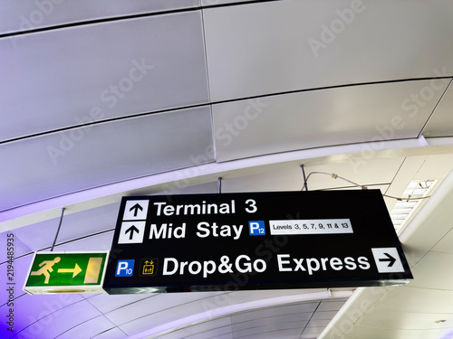 Airport sign for Terminal 3 Mid Stay parking and Drop and Go Express with directional arrows emergency exit icon in a modern curved ceiling concourse