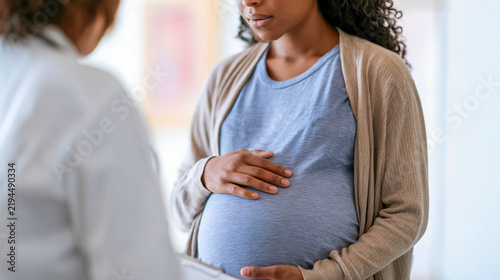 A pregnant woman is at a medical consultation with a doctor; they are discussing the health of the expectant mother and the baby.