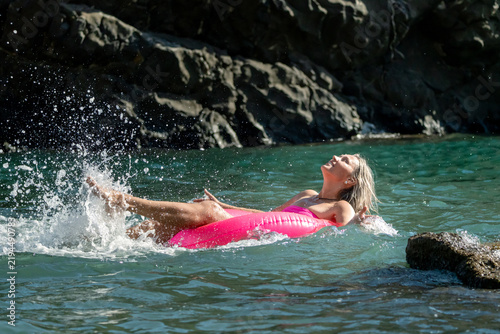 фотографія Blonde woman splashing water while floating on a pink inflatable ring in the sea