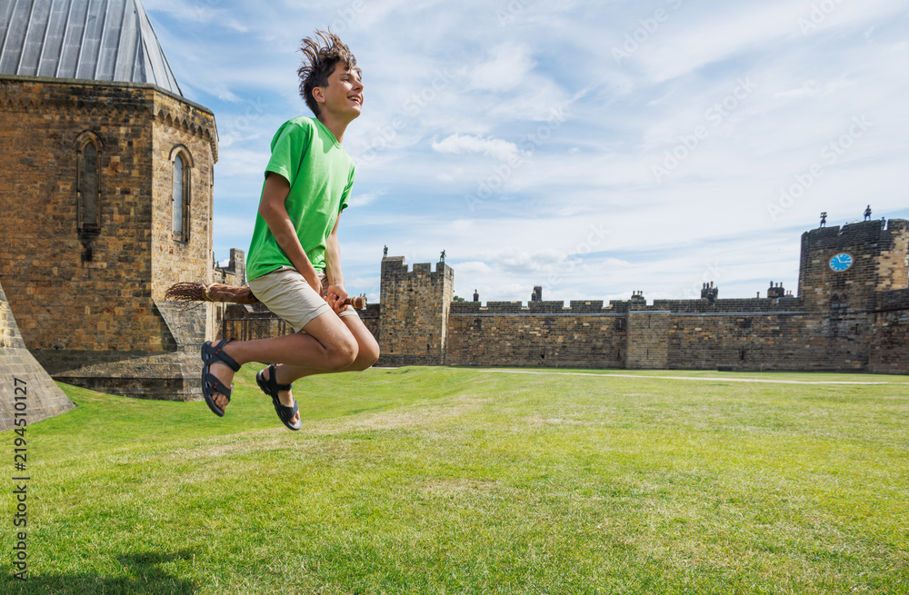 Fototapeta premium Teen have fun joyfully jumping on broomstick in castle courtyard
