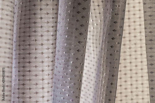 Close-up of translucent sheer curtain fabric with a repeating geometric pattern and soft folds, shallow depth of field.
