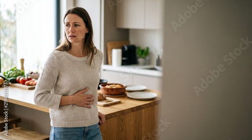 Stomach ache and digestive pain, woman holding belly in kitchen, food intolerance and abdominal discomfort concept, unwell female with indigestion