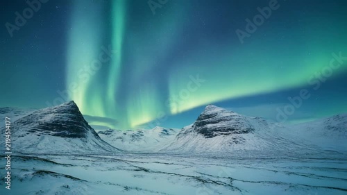 Northern Lights dancing over snow-covered mountains with a frozen landscape during twilight cinematic motion
