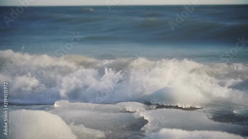Ocean wave breaking against icy shore during daytime with cinematic motion and selective focus