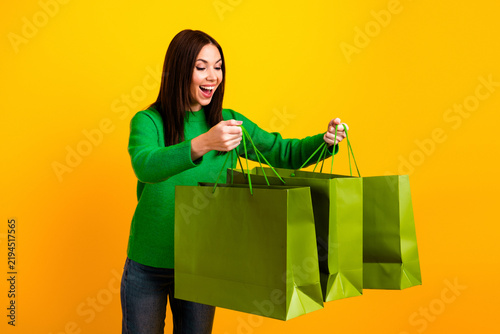 Fotografía Excited woman holding large green shopping bags against a bright yellow backgrou