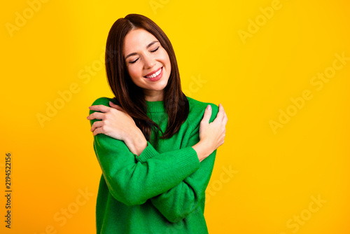 Konstfotografi Young woman hugging herself in green sweater smiling with eyes closed on bright