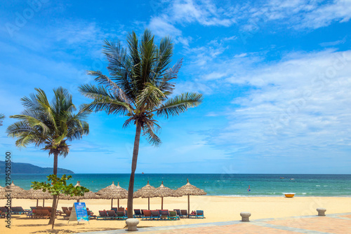 My Khe beach in Da Nang with tall coconut palms, thatched umbrellas, sun loungers, and turquoise sea under blue sky