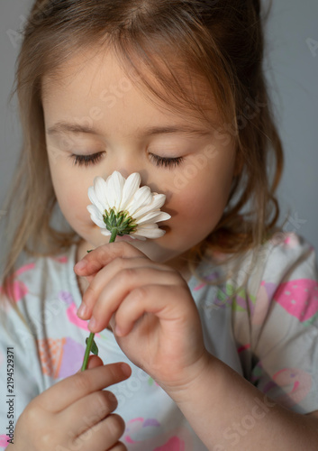Young girl smelling a white daisy flower with closed eyes, peaceful childhood moment in nature, innocence and beauty concept