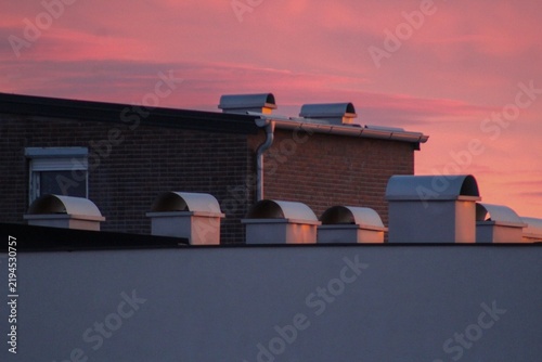 Contemporary residential rooftops with multiple metal ventilation chimneys under a vibrant sunset sky. Ideal image for architecture, construction, housing, engineering, and urban lifestyle concepts.