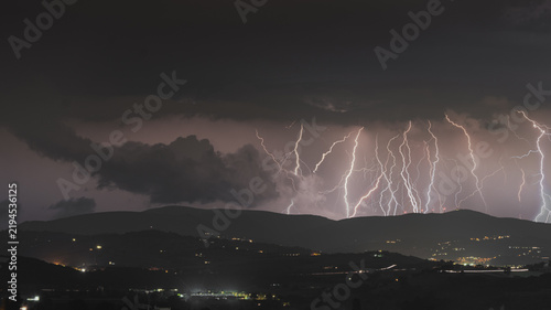 View of multiple lightning bolts striking over the dark hills at night near Corridonia, Marche, Italy.