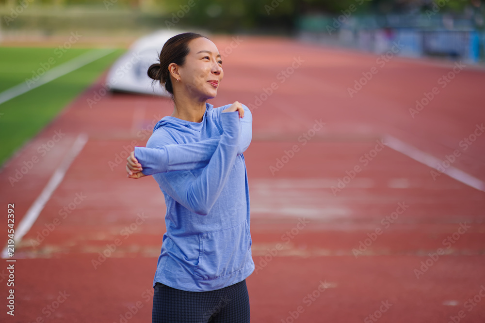 Fototapeta premium Asian woman stretching arms on running track, preparing for outdoor workout, embracing fitness, healthy lifestyle, and wellbeing, finding motivation for daily exercise