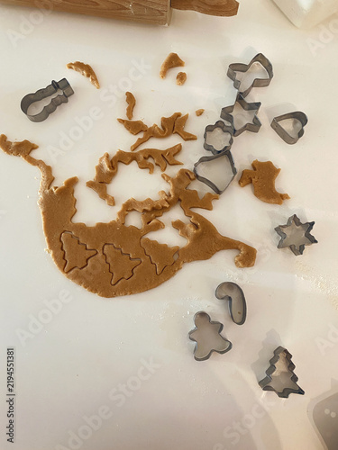 Rolled-out cookie dough on a white countertop features holiday shapes cut out with metal cookie cutters