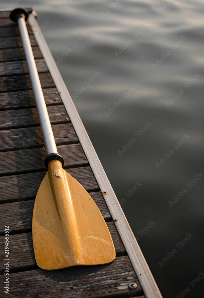 Fototapeta premium Summer vacation and outdoor recreation, yellow kayak paddle resting on a wooden dock by the calm water at sunset for travel and leisure lifestyle