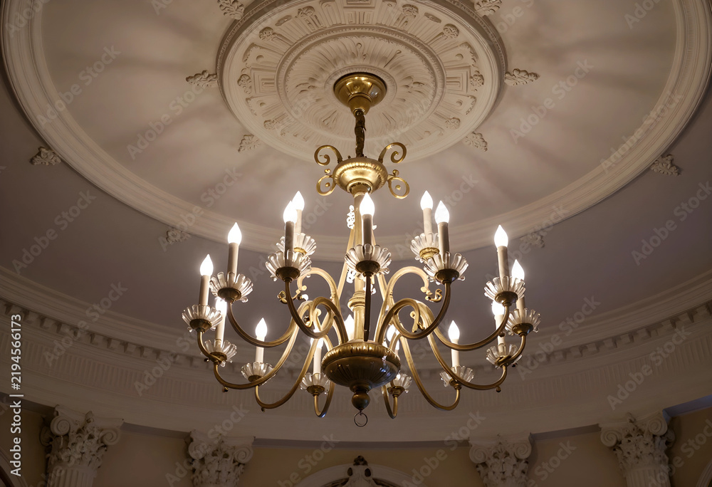 Obraz premium Luxury interior design and opulence, classic gold chandelier hanging from a decorative ceiling medallion in a grand historic building hall