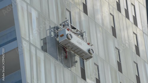 Window cleaning platform hanging on reflective glass facade of a modern skyscraper building in city or business and financial district. Building maintenance unit up keeping and cleaning equipment
