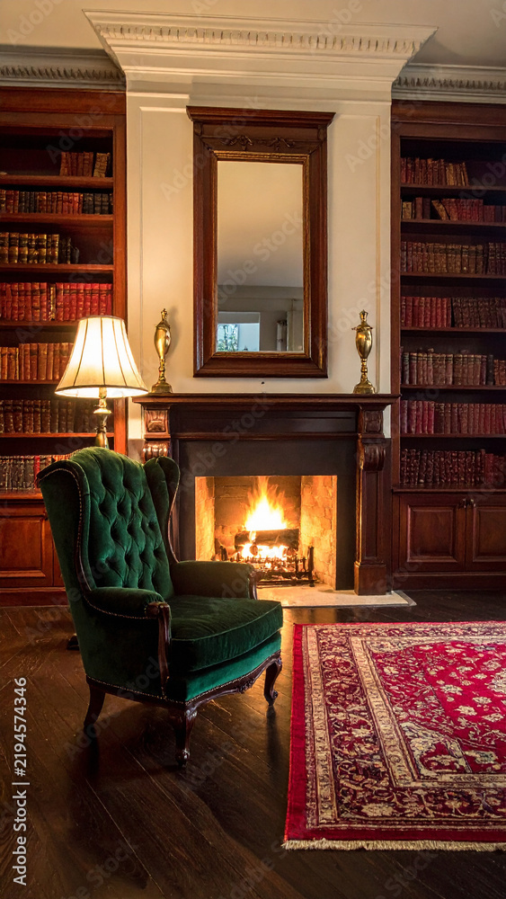 Naklejka premium A cozy, vintage library interior with a green velvet armchair, glowing fireplace, and bookshelves, evoking warmth and intellectual comfort. Nobdy present in this serene, classic study setting.