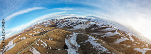 Fotografía An aerial panoramic view of snow-dusted mountain hills with a winding road under a clear blue sky