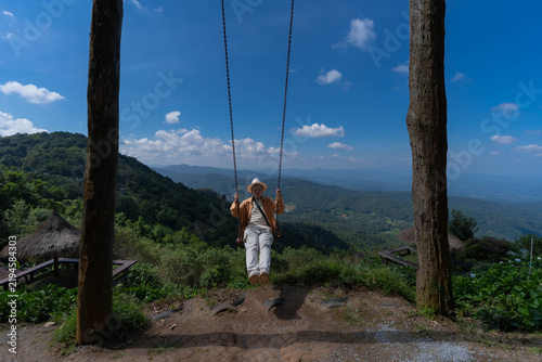 Quadro su tela A man sits on a large wooden swing, admiring the mountain scenery at Mon Jam, Thailand