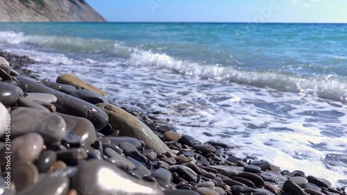 Blue ocean waves splashing on stone beach with mountains in background, coastal landscape, travel destination.