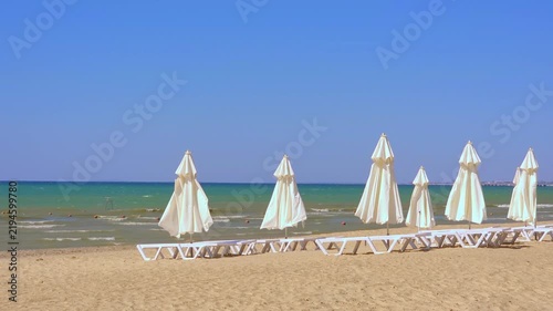 White umbrellas on empty sandy beach by blue sea, summer resort landscape, tropical vacation destination.