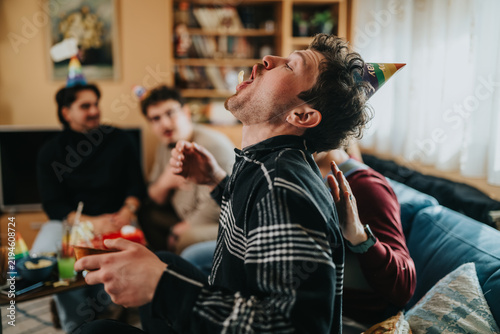 Foto A young man wearing a party hat tries to catch a snack in his mouth while friends watch