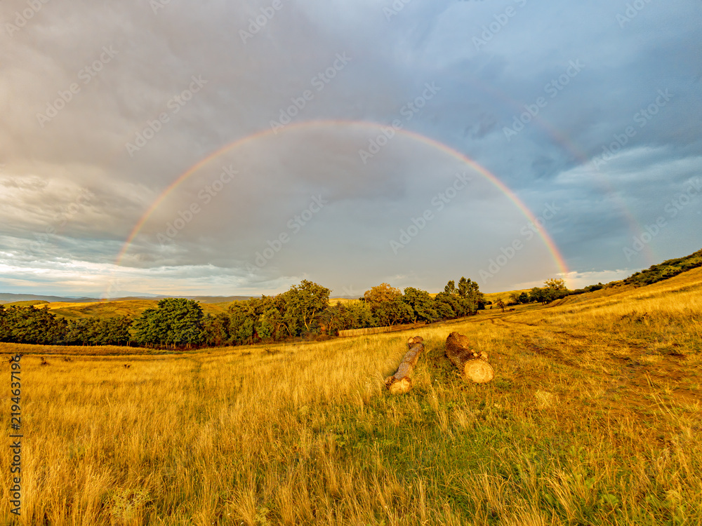 Obraz premium Faint Rainbow Beneath Dramatic Storm Clouds After Rain at Sunrise
