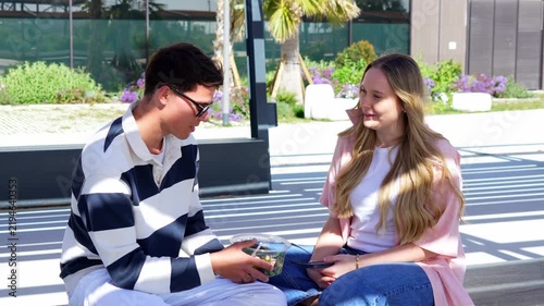 Young couple smiling and eating salad outdoors, enjoying a sunny day together.
