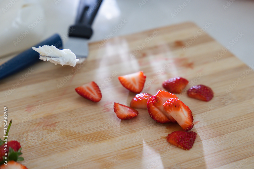 Fototapeta premium Sliced strawberries are glistening on bamboo cutting board near blue-handled utensil, copy space