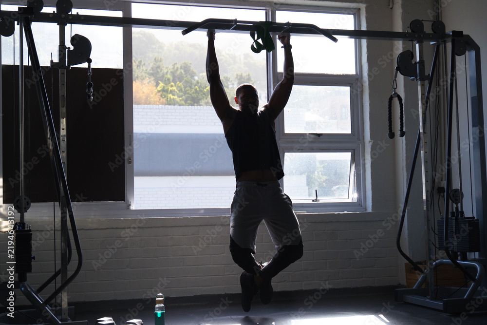 Fototapeta premium Man performing pullup on horizontal bar at gym wearing workout top and shorts with dumbbells