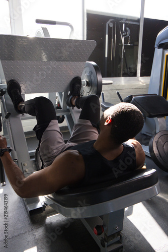 Mid-adult African American man pressing legs on leg-press with plates at gym wearing black tank