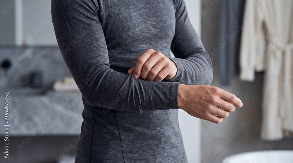 Fototapeta premium Man adjusting a fitted thermal base layer indoors, showing warm functional clothing for cold weather, winter comfort, outdoor activity and seasonal wardrobe