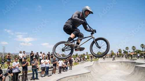 BMX rider performing high jump trick over skatepark bowl in front of crowd