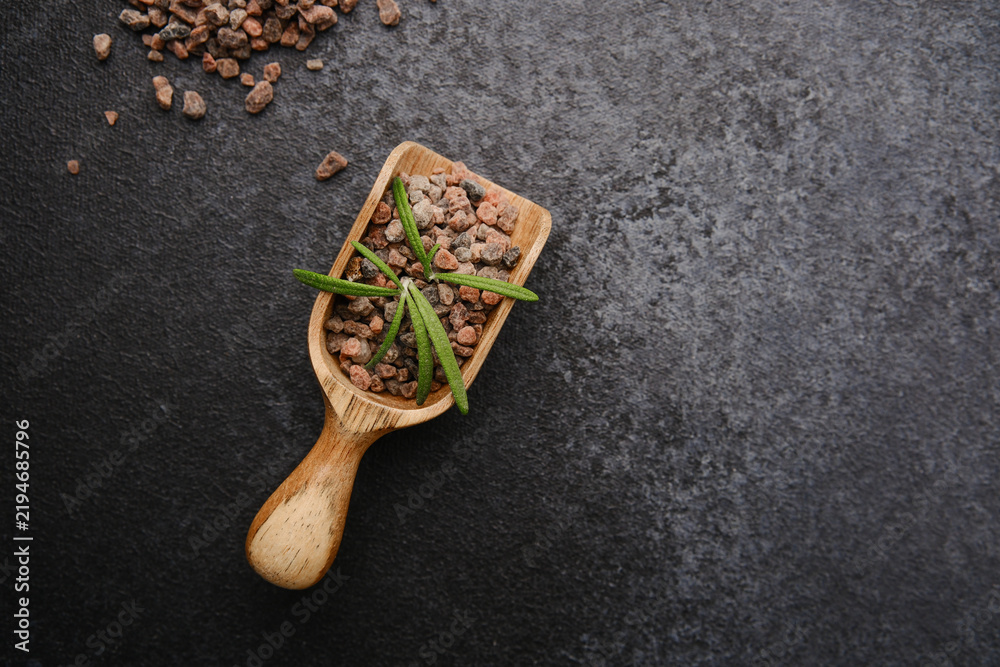Obraz premium Coarse black Himalayan salt crystals in a wooden scoop with rosemary on dark background