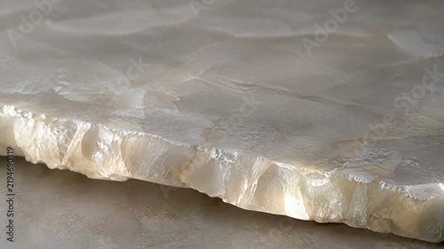 Polished white onyx marble slab with raw chiseled edge, luxury translucent stone texture, elegant quartz mineral surface for interior design