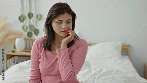 Фотография Woman sitting on bed biting nails, hand to mouth gesture in bedroom building; anxiety reflection solitude concern