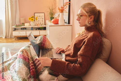 Woman working on laptop in cozy sunlit living room.