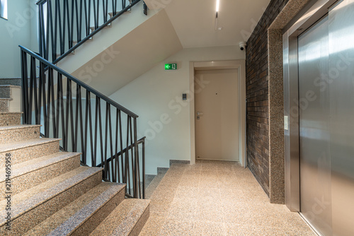 Modern Interior Hallway in Residential Building with Granite Staircase, Elevator, Black Railing and Entrance Door