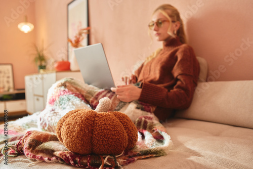 Woman working on laptop with blanket and plush pumpkin