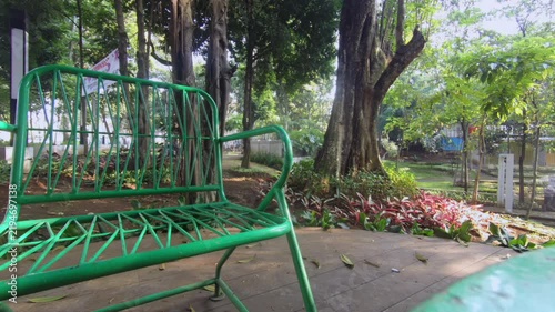 Static view of green metal park bench under large trees in public garden