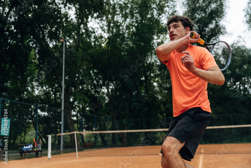 Cuadro en lienzo Male tennis player in orange shirt prepares to hit a forehand shot on a clay cou