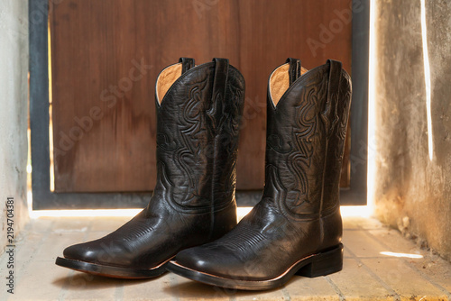 Fotografie Black cowboy boots stand in front of a wooden door