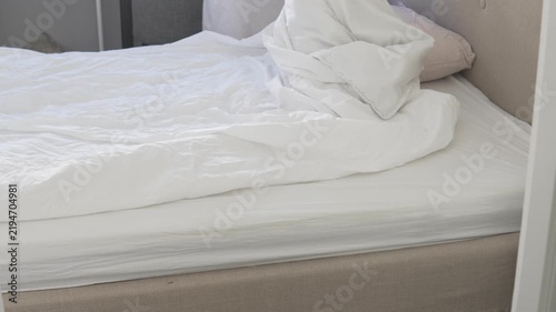 Woman making a bed and putting a duvet into a clean white duvet cover at home. Changing fresh bedding and arranging the bed in a bright bedroom