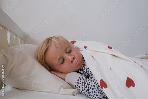 Konstfotografi little girl sleeping peacefully in bed under duvet with red heart print