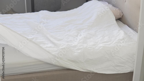Woman spreading and arranging a clean white duvet on a bed while changing fresh bedding in a bright bedroom at home