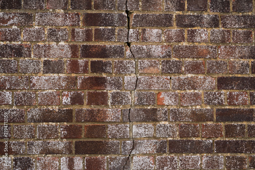 Cracked brown brick wall texture with large vertical structural crack and weathered brickwork