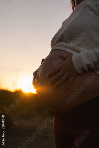Cuadro en lienzo Pregnant belly cradled by hands at golden sunset outdoors, expectant mother in s