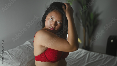 Quadro su tela Woman in red lingerie sits on bed, hand in hair revealing bare breast and thigh in bedroom; sensual intimacy
